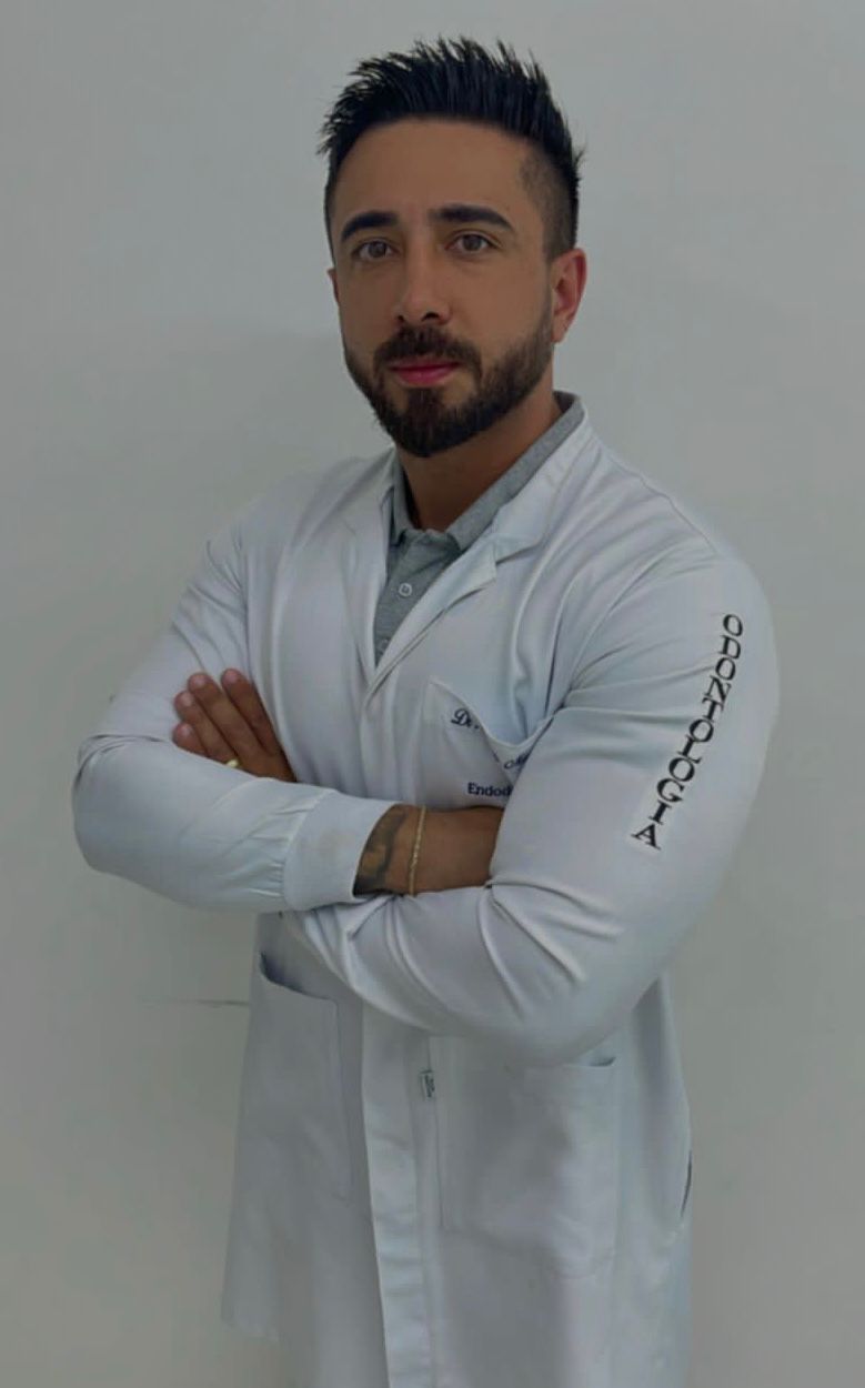 Dr. Thiago dos Santos Matos, cirurgião-dentista, de jaleco e braços cruzados